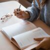 woman in white long sleeve shirt holding pen writing on white paper